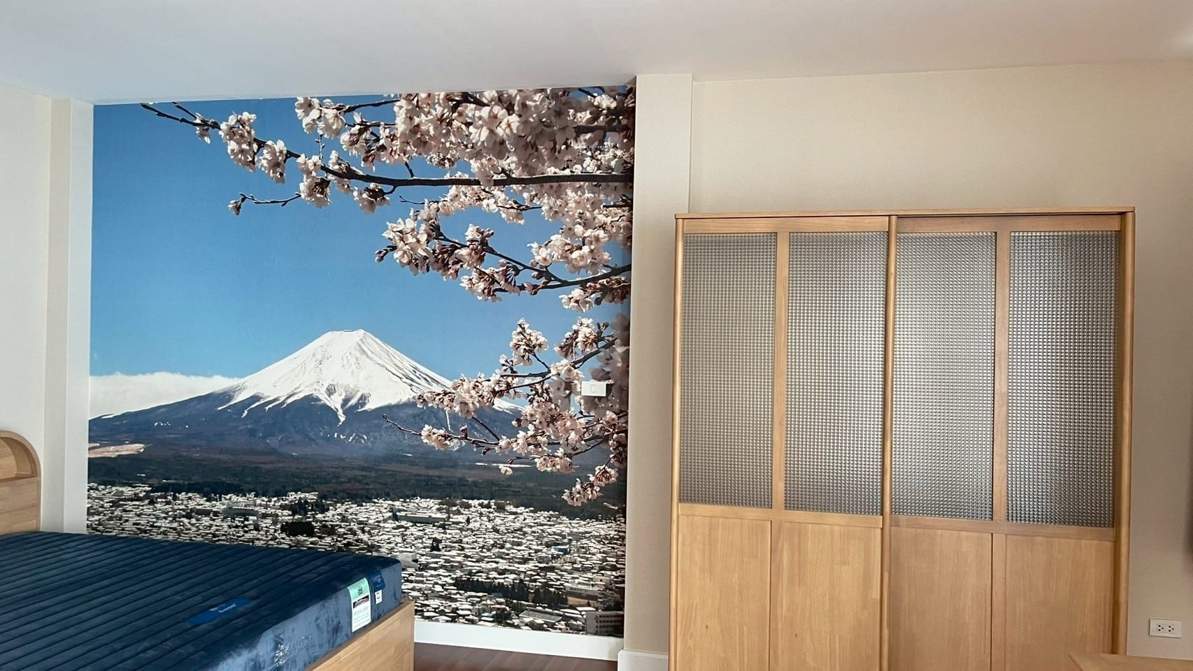 Mount Fuji and cherry blossom mural on a bedroom wall beside a wooden wardrobe